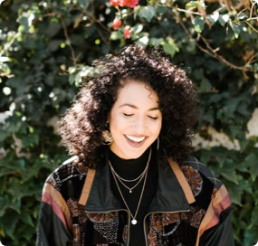 Young woman with curly hair and jacket smiling outdoors