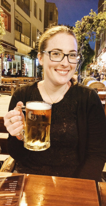 Woman in her 30s smiling on the street, evening, holding a beer