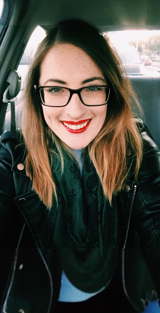 Woman in her 30s, red lipstick, glasses, taking a selfie and smiling