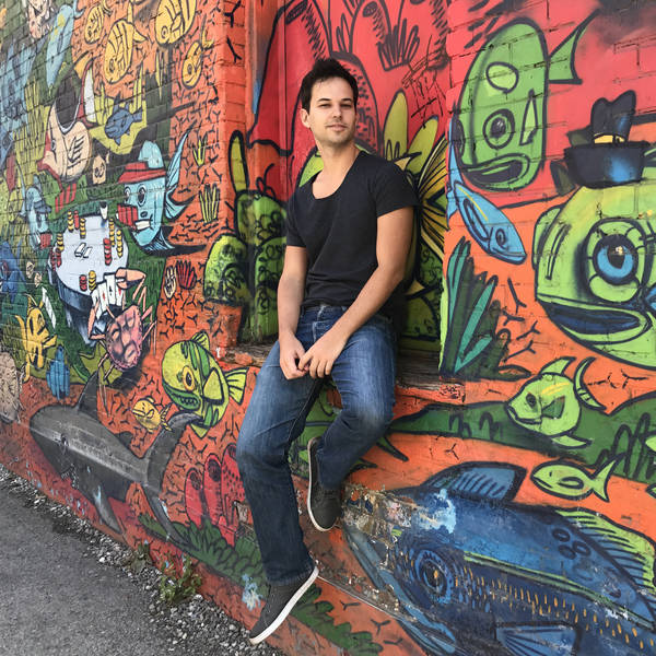 Man in a black shirt and jeans, standing against a background of street art